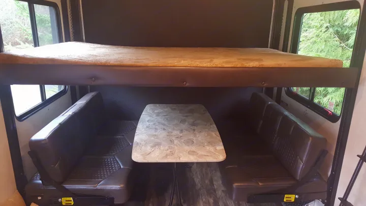 Inside this RV rental: a flexible living space with a comfy dinette table and seats, topped by a bunk bed.. Jayco Octane 2019