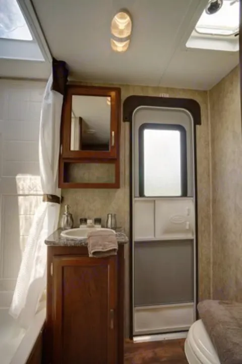 This RV rental bathroom features a tub, vanity, and entry door, showing its compact but functional design.. Keystone Passport 2014