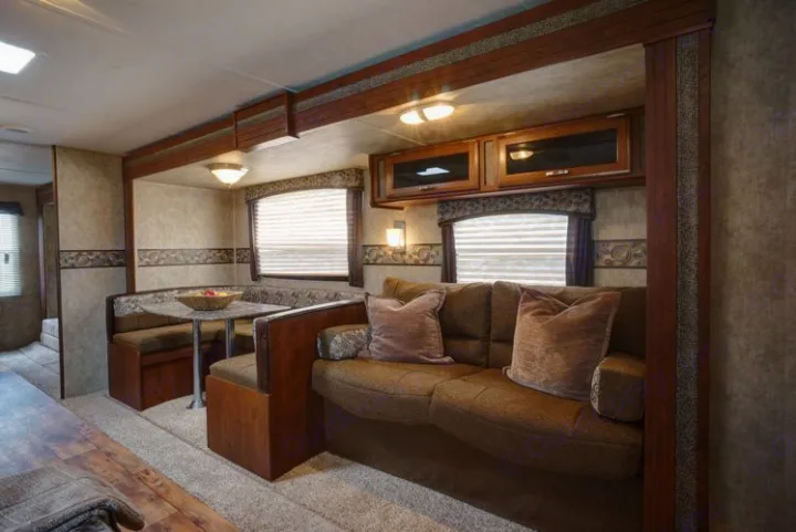 Spacious RV rental interior featuring a comfortable brown sofa with pillows and a booth dinette. Ideal for travel adventures.. Keystone Passport 2014