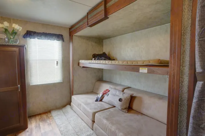 Cozy RV rental interior with bunk beds, a convertible sofa, and a window. Ideal for compact travel adventures.. Keystone Passport 2014