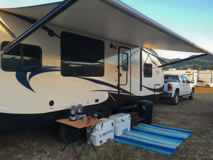 An RV rental is set up with an extended awning, outdoor table, coolers, and mat, ready for camping.. Forest River Evo 2017
