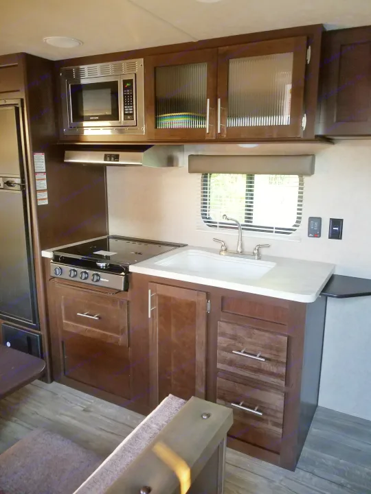 RV rental interior featuring a well-equipped kitchen: microwave, stove, sink, dark wood cabinets, and light countertop.. grey wolf bunkhouse 2018