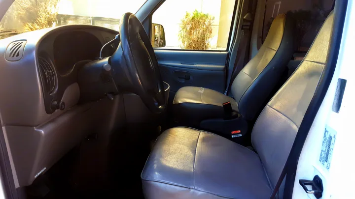 Interior of an rv rental van. View of grey driver's and passenger's seats, steering wheel, and dashboard from the front.. Ford E350 2000