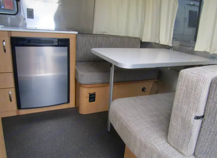 RV rental interior: A compact kitchen with a stainless steel fridge, plus a cozy dinette with upholstered seating.. Airstream Sport 2015
