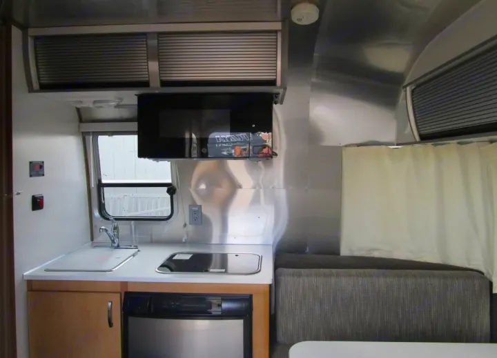 Spacious rv rental interior with a modern kitchen (microwave, sink, stove, fridge) and comfortable dinette seating.. Airstream Sport 2015