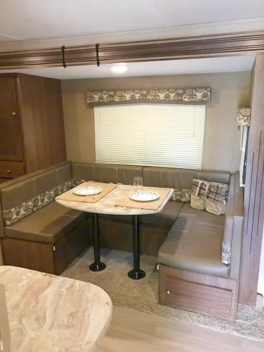 Inside this RV rental: A well-appointed dinette area with grey upholstered seating, an oval table, and a large window.. Coleman Lantern 2018