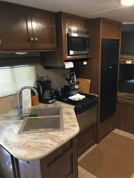 RV rental kitchen featuring a microwave, refrigerator, stove, sink, and ample wood cabinetry for comfortable living.. Coleman Lantern 2018