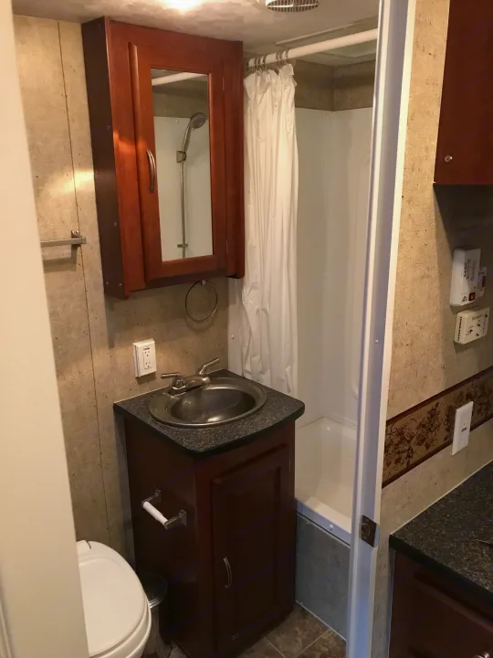 Compact RV rental bathroom featuring a drawn shower curtain, a sink, and toilet, with a wooden medicine cabinet and mirror.. Forest River Wildwood 2011