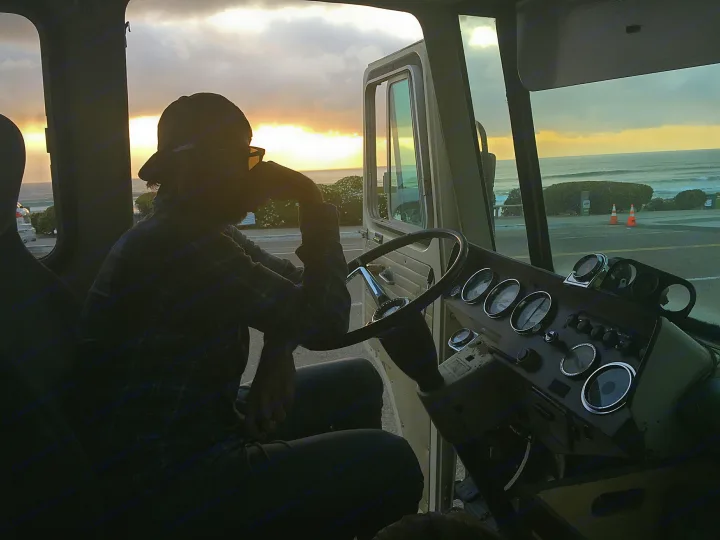 Scenic ocean sunset from an RV rental's driver seat, with a person silhouetted and dashboard details visible.. Clark Cortez 1966