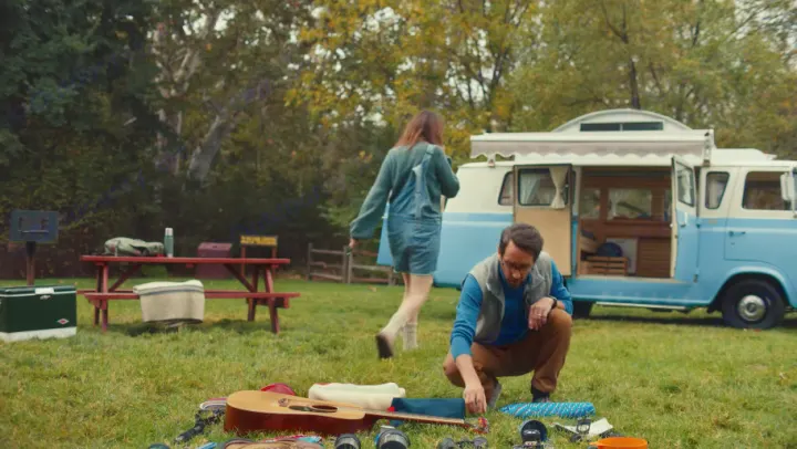 Enjoying an RV rental trip! A man organizes gear next to a retro camper van at a scenic campsite.. Ford Econoline 1966