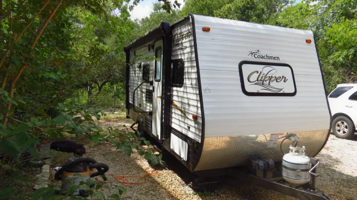 White Coachmen Clipper rv rental travel trailer parked on gravel in a shady, treed campsite, ready for your outdoor adventure.. Coachmen Clipper 2016