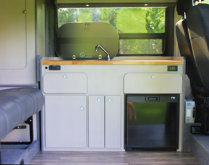 Inside an RV rental: Compact kitchen with sink, fridge, cabinets, and a side bench for convenient travel.. Dodge Promaster 2017