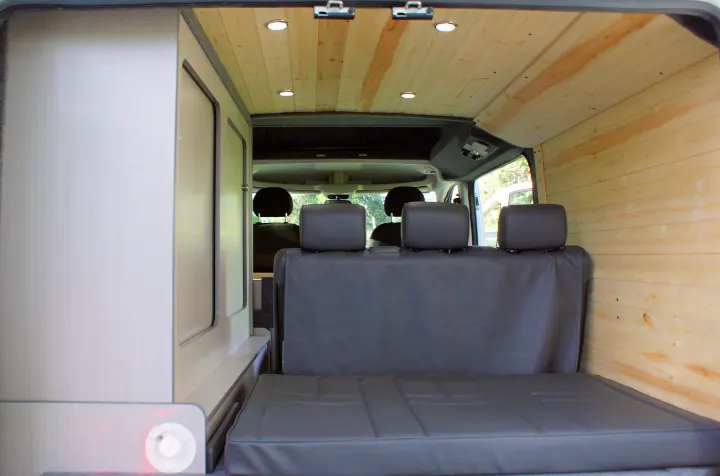 Inside an RV rental: light wood paneling, gray folding bed/seating, and light-colored interior cabinets.. Dodge Promaster 2017