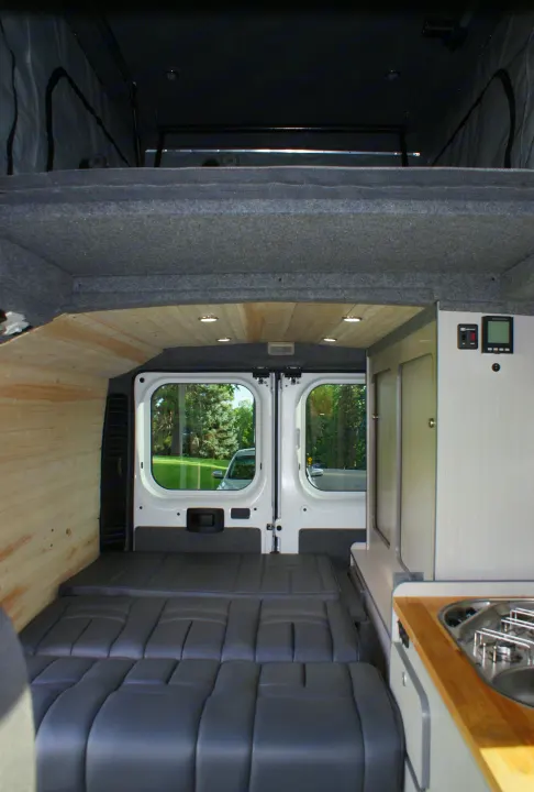 Spacious RV rental interior showing a convertible bed, overhead bunk, wood ceiling with lights, and a full kitchen.. Dodge Promaster 2017