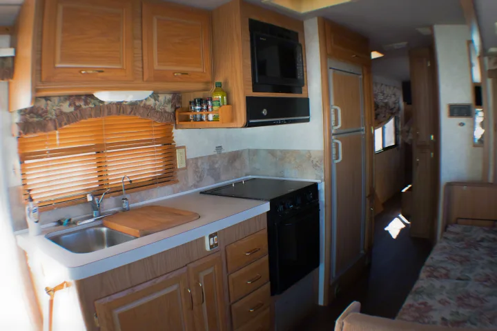 Explore this cozy rv rental kitchen featuring wood cabinets, a sink, stove, microwave, and fridge, perfect for your adventures.. Fleetwood Bounder 1999