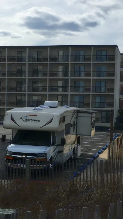 White Coachmen Freelander RV rental with slide-out extended, parked by a multi-story hotel building.. Coachmen Freelander 2018