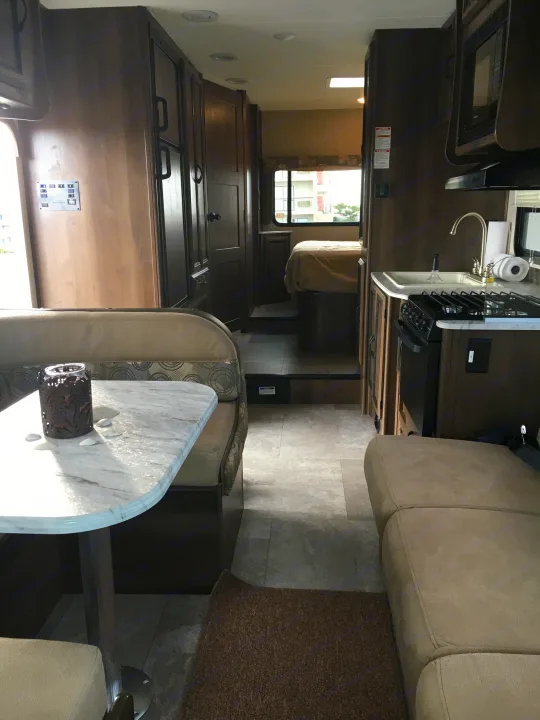 Explore this clean rv rental interior, showcasing a bright dining area, well-equipped kitchen, and comfortable bedroom.. Coachmen Freelander 2018