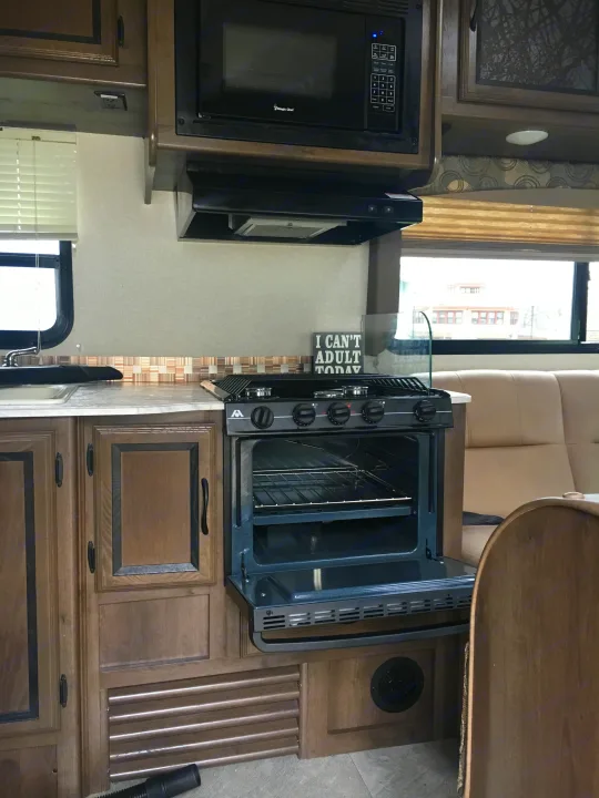 Well-equipped RV rental kitchen featuring a microwave, gas range with an open oven, sink, & cabinets for travel cooking.. Coachmen Freelander 2018