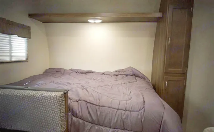 RV rental bedroom: cozy bed with purple comforter, window, and cabinet for comfortable travels.. Riverside Rv Dream 175BH 2018