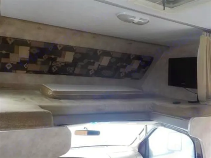 Interior view of an RV rental: a cozy cab-over bunk with mattress and wall-mounted TV.. Gulf Stream Yellowstone 2009