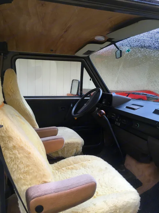 An inviting rv rental campervan interior, featuring plush sheepskin seats, wood panel ceiling, and a rainy windshield view.. Volkswagen Vanagon 1985