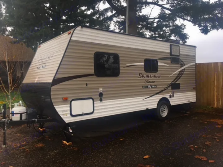 A tan and white Sportsmen Classic travel trailer with propane tanks, a great option for an rv rental, parked on a paved lot.. KZ SPORTSMEN 2017