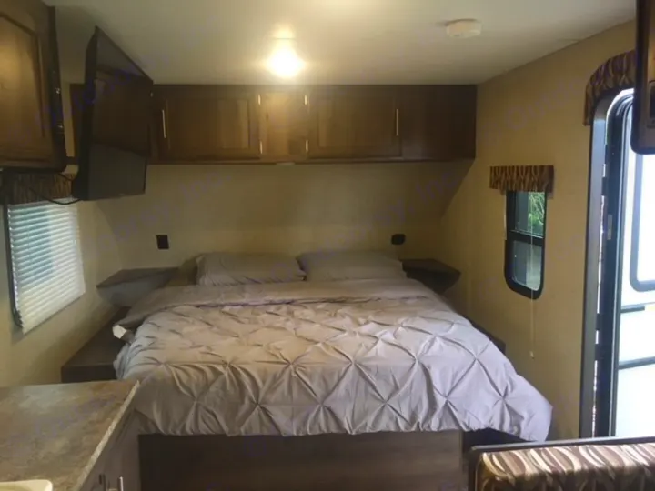 Cozy RV rental bedroom featuring a queen bed, TV, window, and overhead storage cabinets, ideal for a comfortable stay.. KZ SPORTSMEN 2017