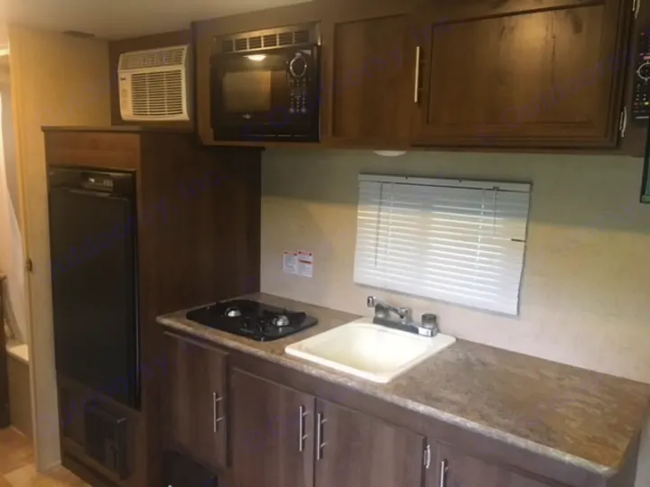 This RV rental's compact kitchen includes a sink, stove, microwave, fridge, and AC unit, ideal for your next trip.. KZ SPORTSMEN 2017