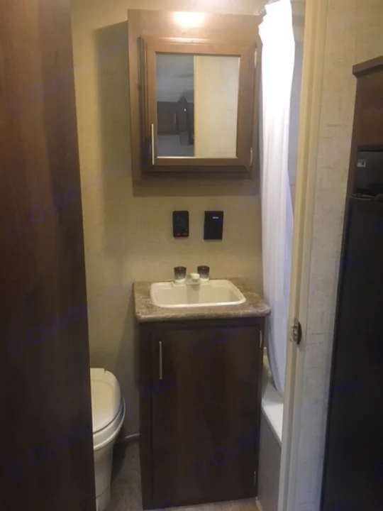 Compact RV rental bathroom featuring a vanity with sink, mirror, toilet, and utility controls.. KZ SPORTSMEN 2017