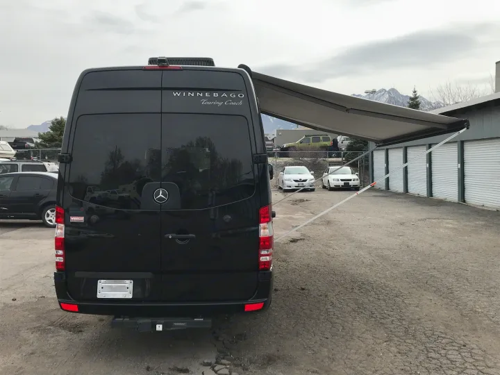 This black Winnebago Touring Coach RV van, perfect for RV rental, has its side awning extended, parked in a lot.. Winnebago Era 2014