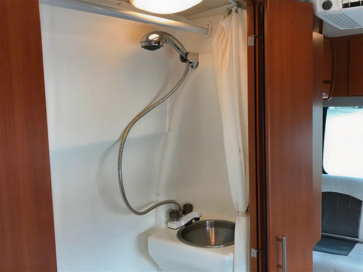 A clean, compact RV rental bathroom with a chrome handheld shower, stainless steel sink, and white privacy curtain.. Winnebago Era 2014