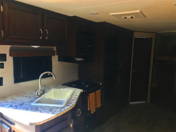 Modern RV rental kitchen with dark cabinetry, light marbled counters, sink, stovetop, and microwave for your travels.. Jayco JAY FLIGHT SLX 287 BHS 2018