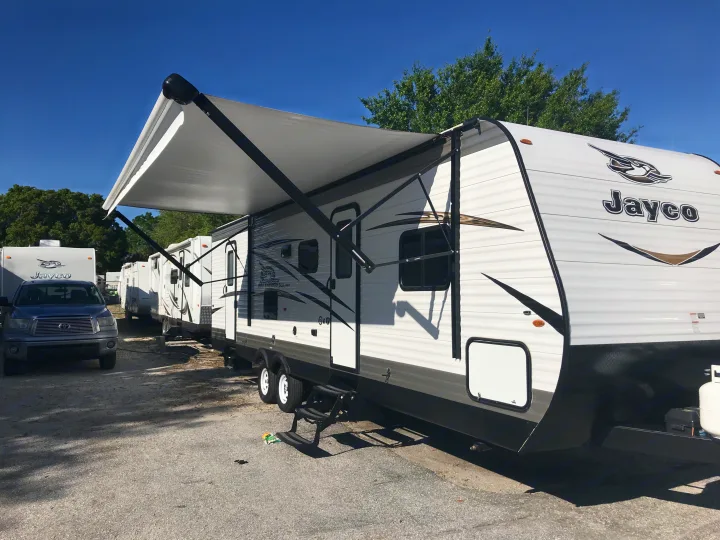 Sunny day at an rv rental lot, featuring Jayco travel trailers. One RV has a large extended awning; a pickup truck is parked.. Jayco JAY FLIGHT SLX 287 BHS 2018