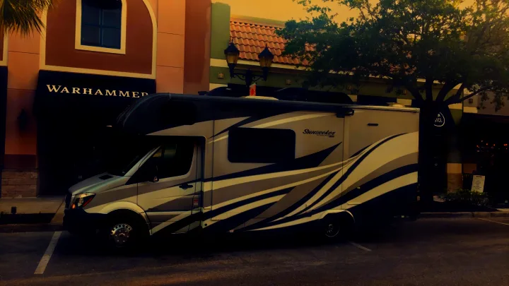 A sleek grey and white Sunseeker rv rental, a large motorhome, is parked roadside near shops like Warhammer and Clean Juice.. ForestRiver Sunseeker 2018