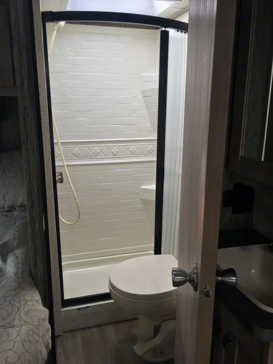 Inside an RV rental: White shower, toilet, and vanity sink in a compact, functional bathroom setup.. ForestRiver Sunseeker 2018