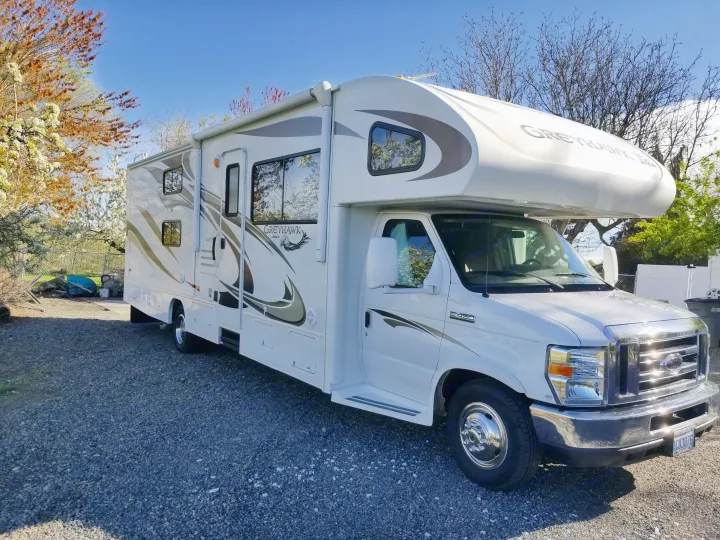 A white Jayco Greyhawk Class C RV with an awning is parked on a gravel lot, ready as an rv rental.. Jayco Greyhawk 2011
