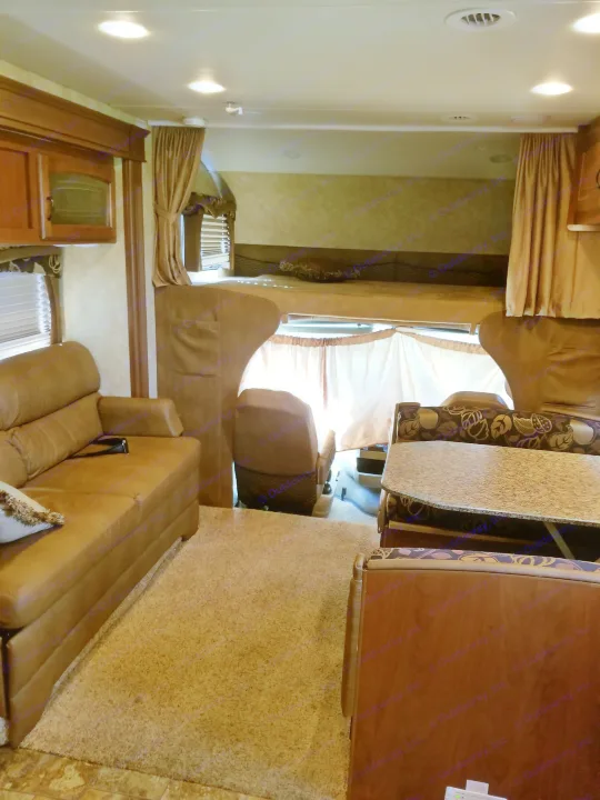Inside an RV rental, showing a brown leather sofa, dinette with patterned cushions, and an upper bunk bed.. Jayco Greyhawk 2011