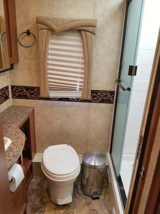 Inside an RV rental bathroom: features a modern toilet, compact sink vanity, glass shower, and a window with decorative valance.. Jayco Greyhawk 2011