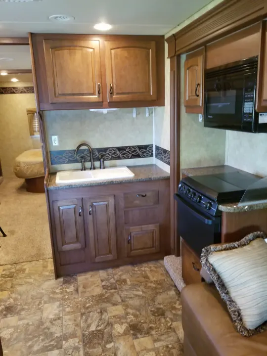 Modern rv rental interior: kitchen with sink, stove, microwave, wood cabinets, tiled floor; cozy bedroom, living area.. Jayco Greyhawk 2011