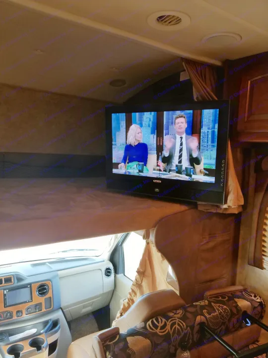 RV rental interior with a TV showing a talk show mounted above a bunk bed, overlooking the driver's cabin.. Jayco Greyhawk 2011