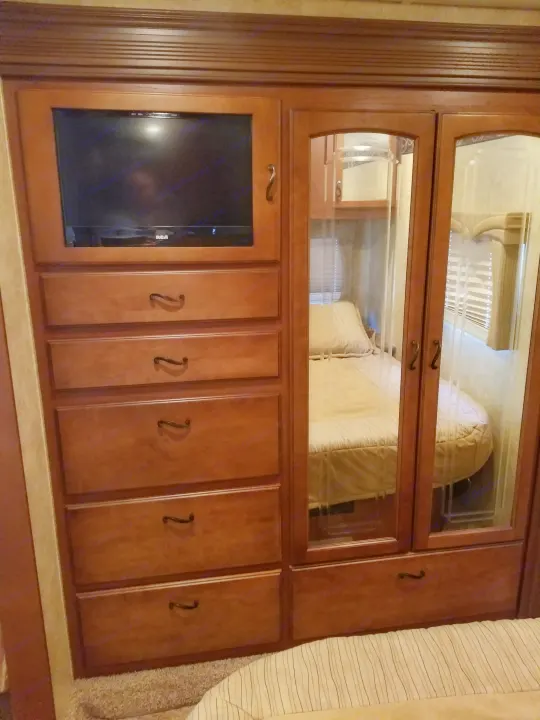 RV rental bedroom with built-in wooden dresser, mounted TV, and mirrored wardrobe reflecting the cozy bed.. Jayco Greyhawk 2011