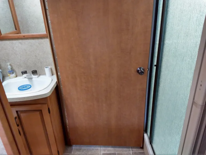 An RV rental bathroom showing a wooden door, a sink with a soap dispenser, and a frosted glass shower enclosure.. Forest River Sunseeker 2013