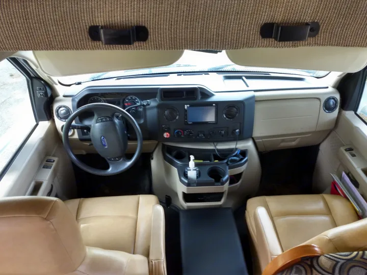 Interior front of an RV rental: beige dashboard, Ford steering wheel, center console with cupholders, and comfortable front seats.. Forest River Sunseeker 2013