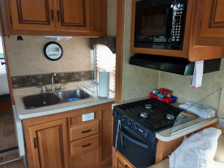 Compact and functional kitchen inside an RV rental, featuring a sink, microwave, stove, and ample cabinet space for cooking needs.. Forest River Sunseeker 2013