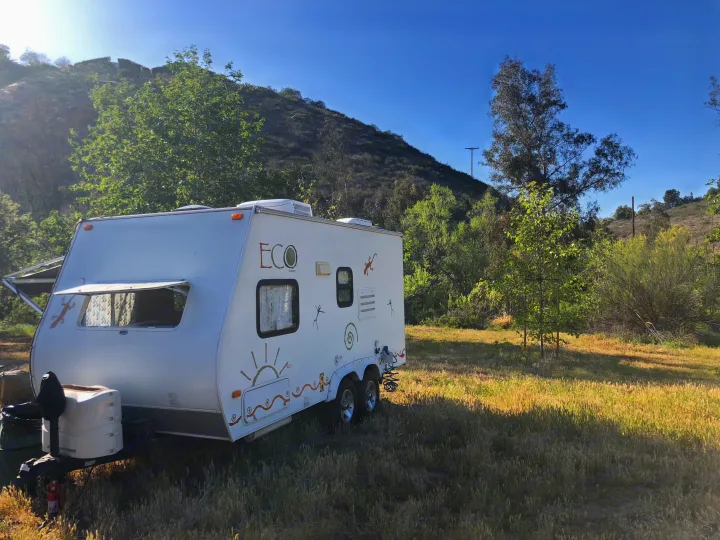 RV rental: White travel trailer with unique decals, parked in a grassy, sunlit natural setting.. Dutchman Eco 2010