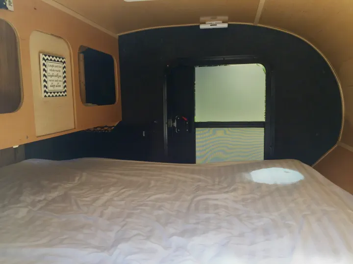 Inside a compact RV rental: a comfy bed, functional storage, a wall sign, and a rear door with a screen.. Other Travel Trailer 2009
