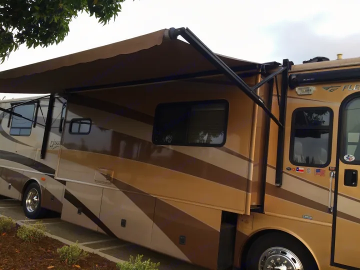 This Class A RV rental, a brown and tan motorhome with an extended awning and slide-out, is ready for adventure.. Fleetwood Discovery 2005