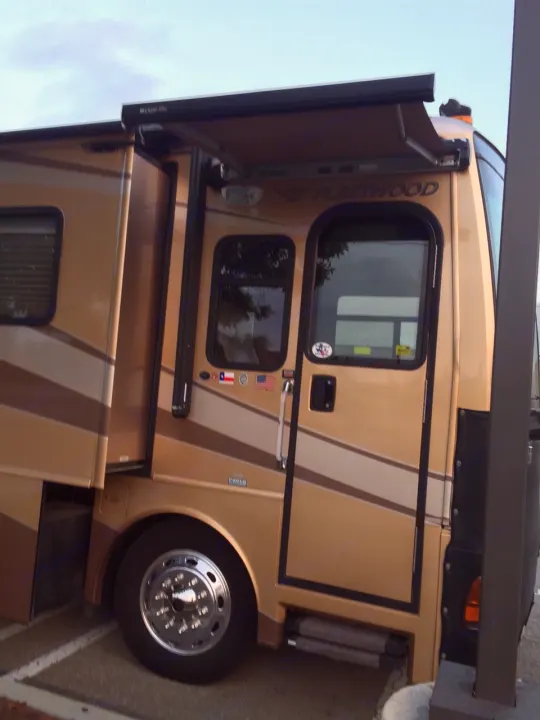 A golden-brown RV rental, a large motorhome with an extended awning, parked for your next travel adventure.. Fleetwood Discovery 2005