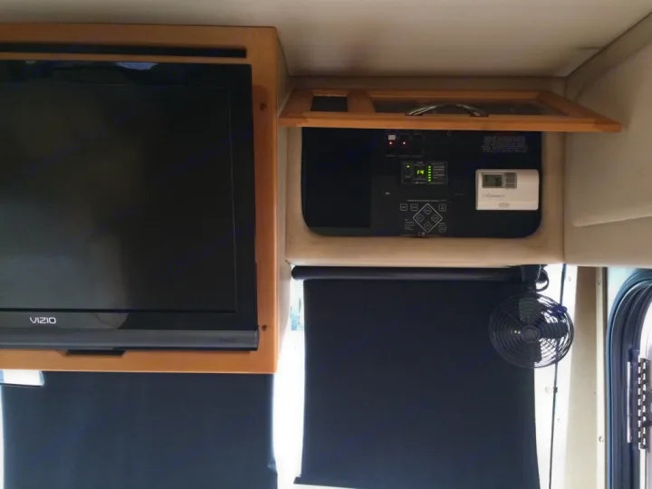 An RV rental interior with a VIZIO TV, overhead power controls, a digital thermostat at 76°, shades, and a fan.. Fleetwood Discovery 2005