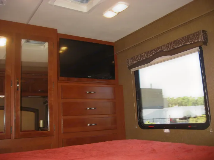 Inside an RV rental bedroom: cozy space with wood cabinets, TV, and a window offering a view.. Thor Motor Coach Chateau 29G 2016